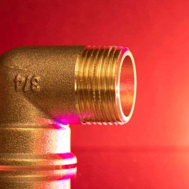 Close-up of a shiny brass pipe elbow fitting against a vibrant red backdrop, showcasing industrial elegance.