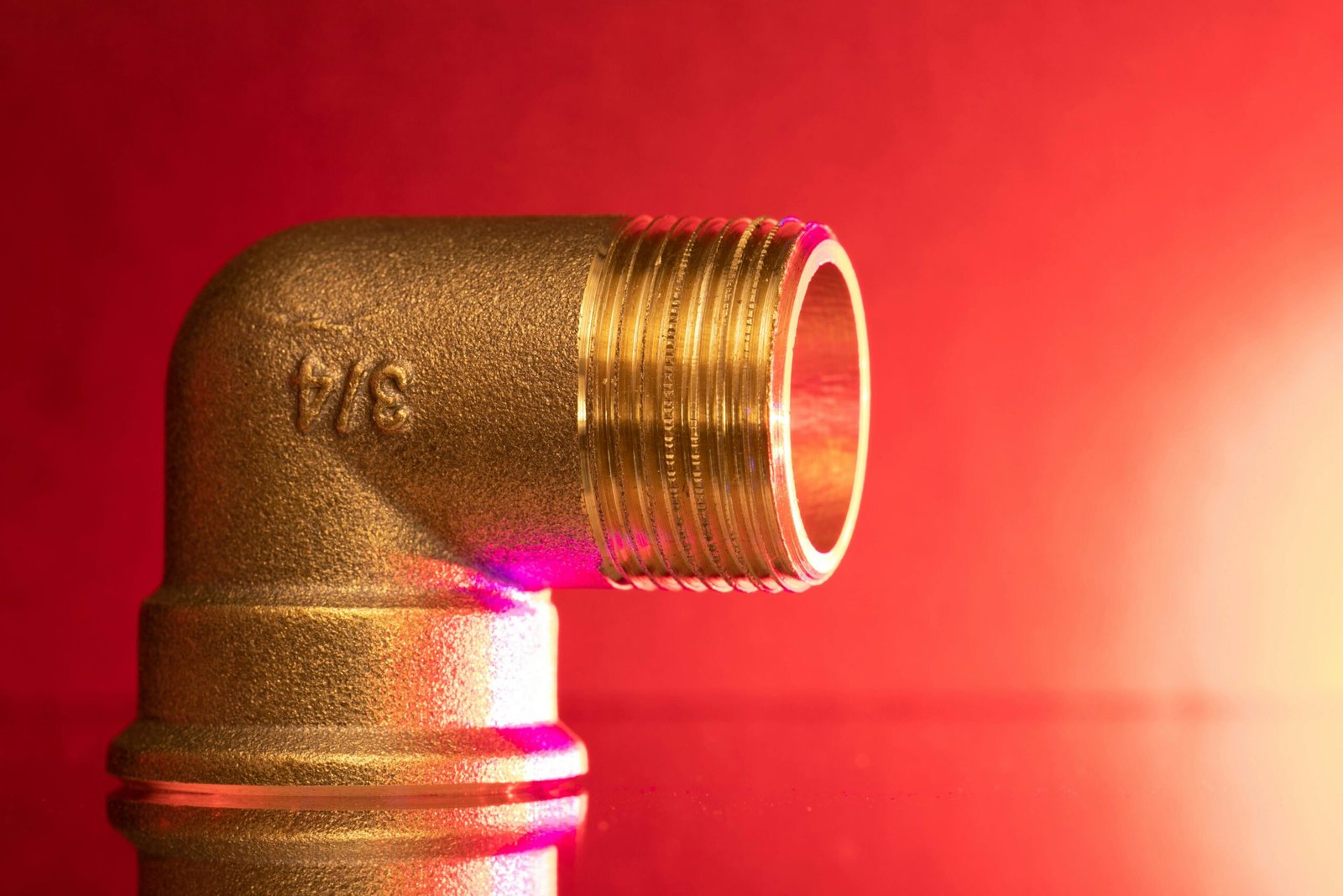 Close-up of a shiny brass pipe elbow fitting against a vibrant red backdrop, showcasing industrial elegance.